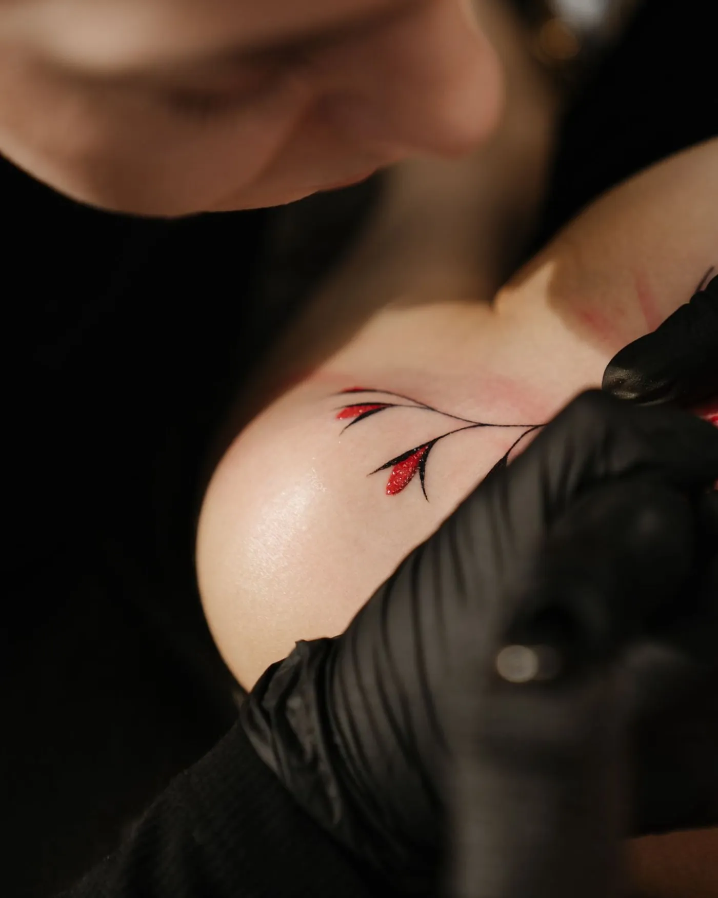 A botanical stem following the line of the collarbone, with a single red bud.