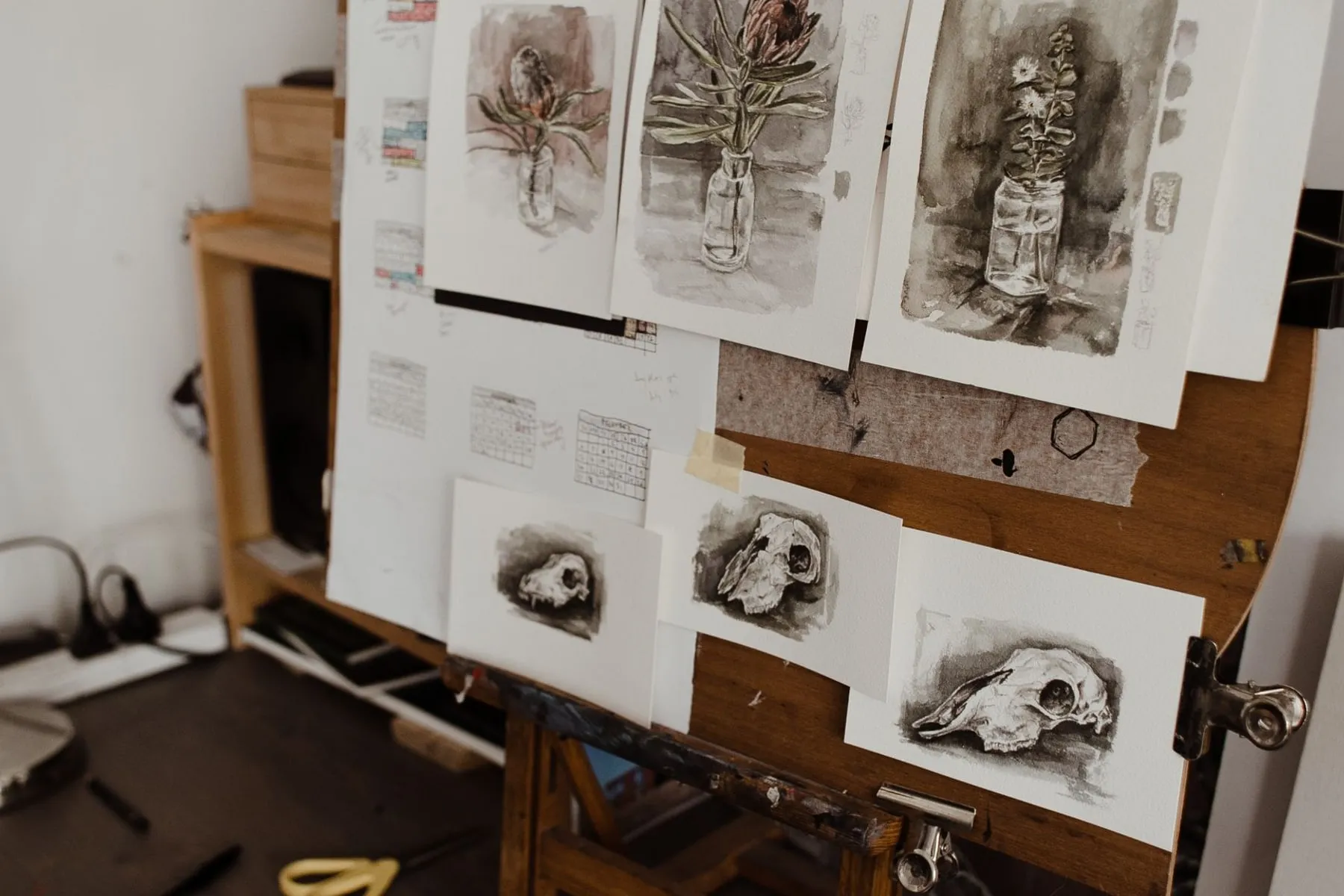 An easel of reference prints and framed drawings standing beside the drawing desk.