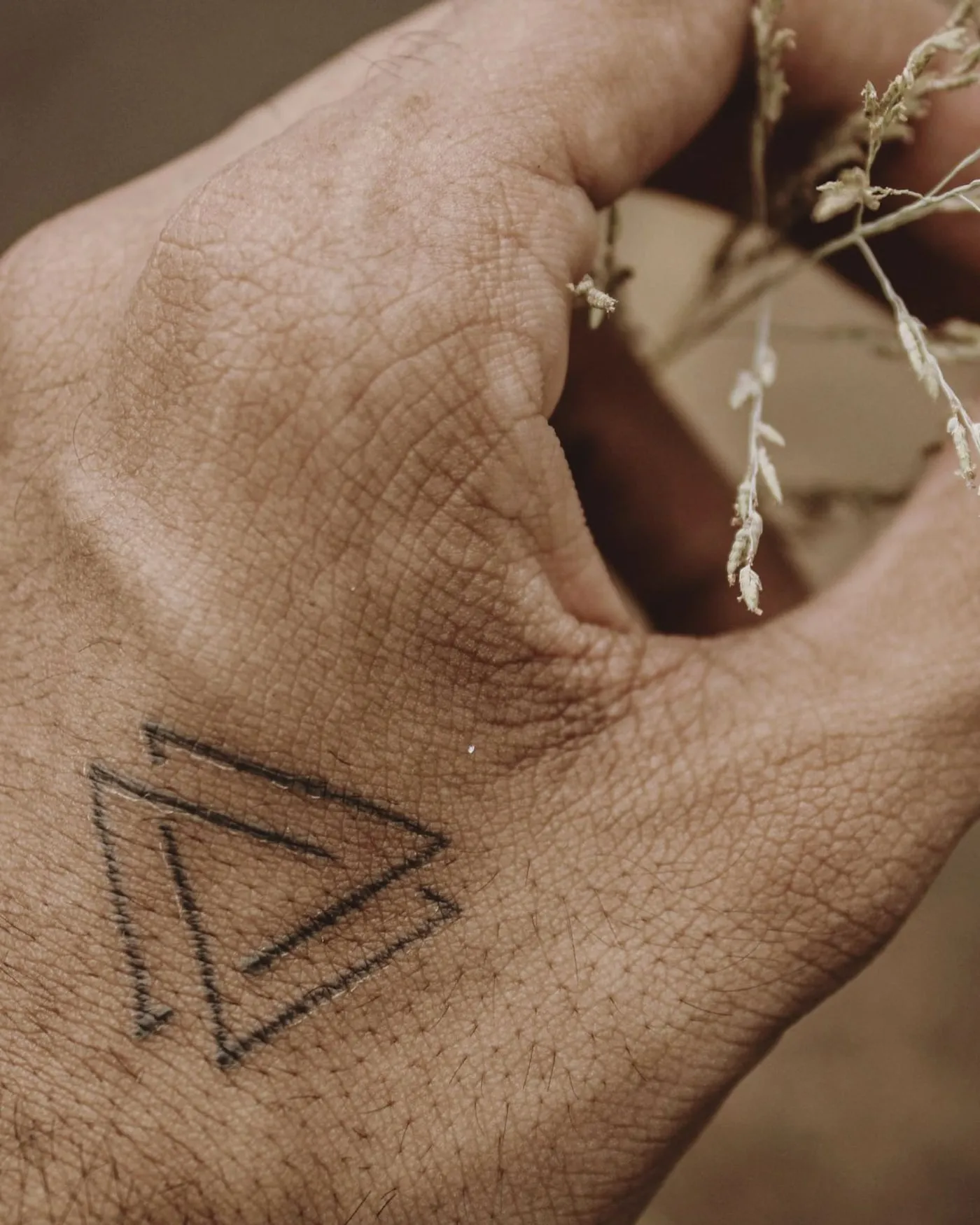 A small geometric fine-line tattoo on the back of the hand.